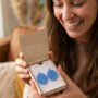Lachende vrouw toont geopende houten doosje met blauwe oorbellen als cadeau
