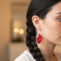 Close-up van het oor van een vrouw met een dikke, gevlochten staart die een rode oorbel in de vorm van een gedetailleerd anatomisch menselijk hart draagt.