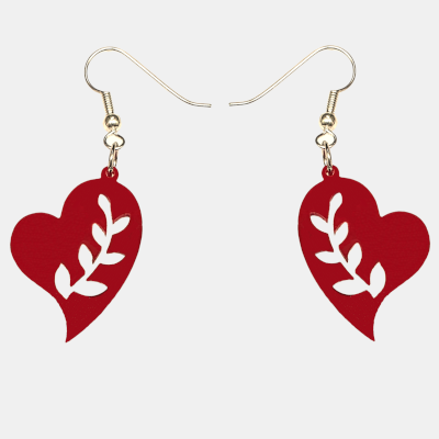 Close-up van een rood, hartvormig oorbel met uitgesneden bladmotief, hangend aan een zilverkleurige oorhaakje in het oor van een vrouw met blond haar. Detailopname van de oorbel en het haar.