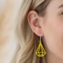 Gele geometrische oorbellen in de vorm van een diamant/edelsteen, gedragen door een blonde vrouw met golvend haar. De oorbellen hebben een zilverkleurige haak.
