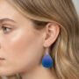 Close-up van een blond model van de zijkant die een matte druppelvormige epoxy oorbel draagt met een kleurverloop van paars naar blauw zonder glans.