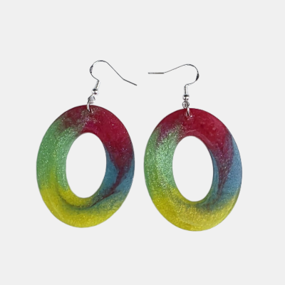 Paar grote handgemaakte ovale epoxy oorbellen met een abstract en kleurrijk verloop van roze, groen, geel en blauw voorzien van sprankelende glitters op een witte achtergrond.