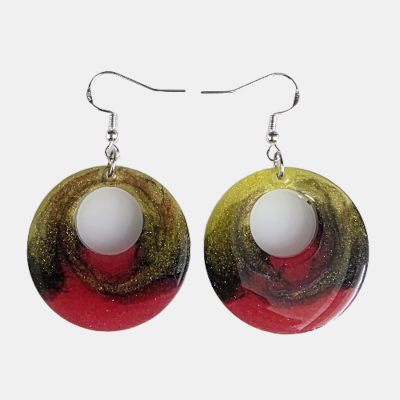Paar handgemaakte ronde epoxy oorbellen met een artistiek patroon van rood, goud en zwart met een opvallend open rond detail in het midden.