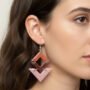 Close-up van een model met donker haar van de zijkant gezien die een geometrische resin oorbel draagt in de kleuren terra, bruin en lichtroze met glitters.