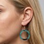 Gedetailleerde close-up van een vrouwelijk model met blond haar en een aqua-blauw met zwarte marmeren epoxy earring.