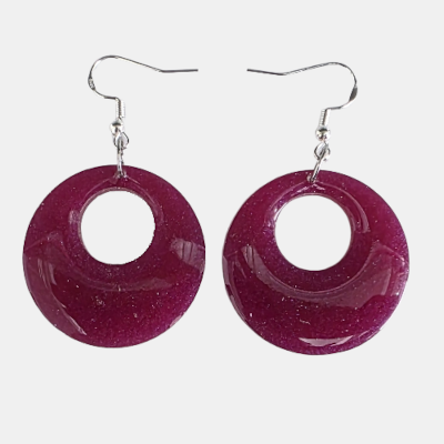 Twee handgemaakte epoxy oorbellen bestaande uit ovale hangers met een goudgroen kleurverloop en ronde fuchsia paarse hangers met glitters op een witte achtergrond