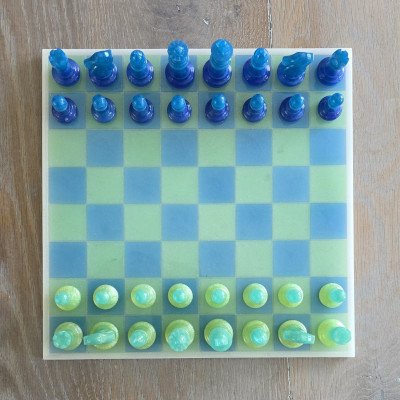 Modern handgemaakt schaakbord van hars in transparant blauw en limegroen op houten ondergrond bovenaanzicht.