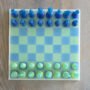 Handgemaakt epoxy schaakbord met blauwe en limegroene transparante schaakstukken in schuin vooraanzicht op houten tafel.