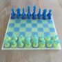 Handgemaakt epoxy schaakbord met blauwe en limegroene transparante schaakstukken in schuin vooraanzicht op houten tafel.