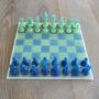 Handgemaakt epoxy schaakbord met blauwe en limegroene transparante schaakstukken in schuin vooraanzicht op houten tafel.