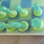 Handgemaakt epoxy schaakbord met blauwe en limegroene transparante schaakstukken in schuin vooraanzicht op houten tafel.