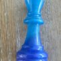 Detailopname van een handgemaakte blauwe epoxy schaakstuk koning met glinstering op een houten achtergrond.