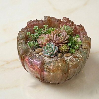 Bovenaanzicht van een decoratieve schaal van glitterende kunsthars gevuld met verschillende soorten Echeveria vetplanten en fijne kiezels op een marmeren ondergrond.