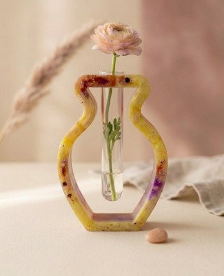 Handgemaakt geel epoxy vaasje met glazen reageerbuis en een roze bloem op een beige ondergrond.