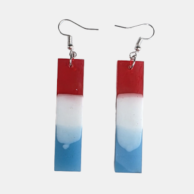Handgemaakte rechthoekige hars oorbellen met een verticaal kleurverloop in rood, wit en blauw aan zilverkleurige oorhaakjes.