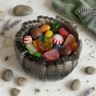 Handgemaakt zwart epoxy snoepschaaltje met gouden glitters gevuld met kleurrijk snoepgoed op een marmeren ondergrond met lavendel decoratie