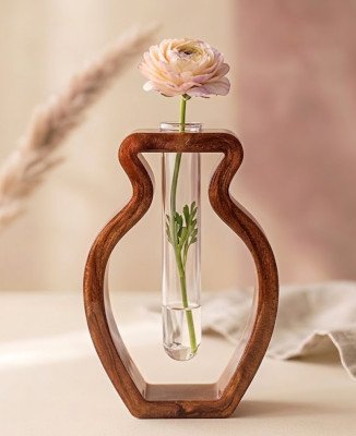 Een moderne epoxyvaas in de vorm van een fles met een glazen reageerbuis, gevuld met water en één roze ranunculusbloem en blad, geplaatst tegen een zachte achtergrond.