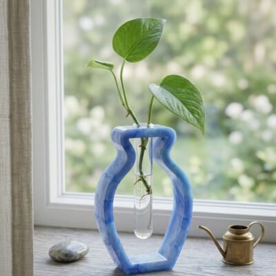 Blauwe handgemaakte epoxy vaas in organische vorm met glazen reageerbuis voor stekjes op een houten vensterbank.